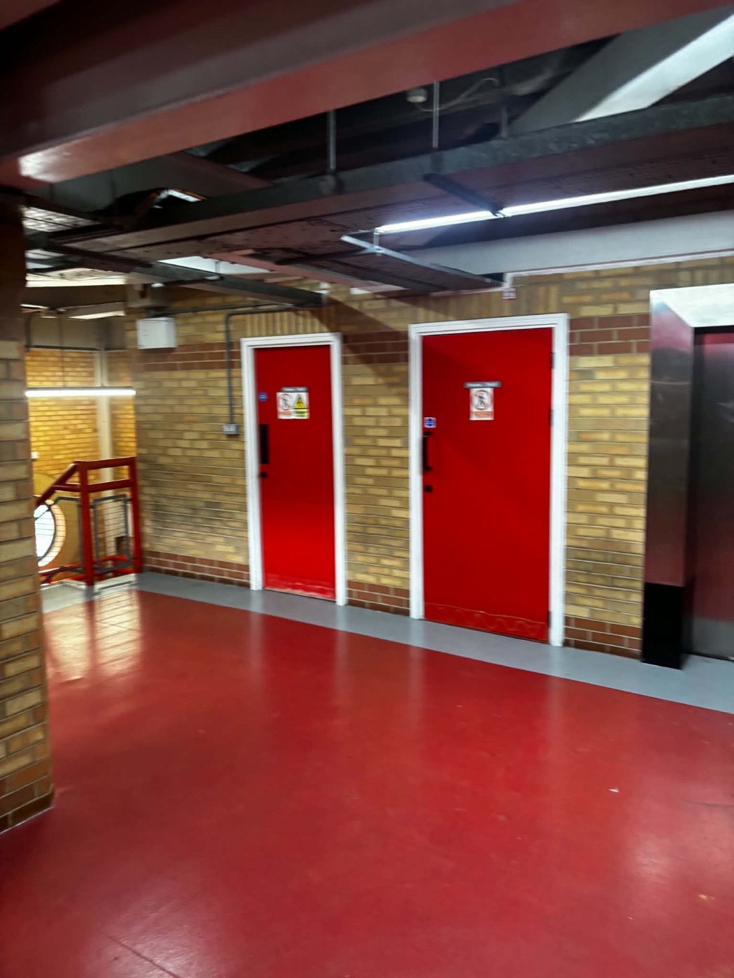 Paired red doors and white frames along a concourse wall at Anfield