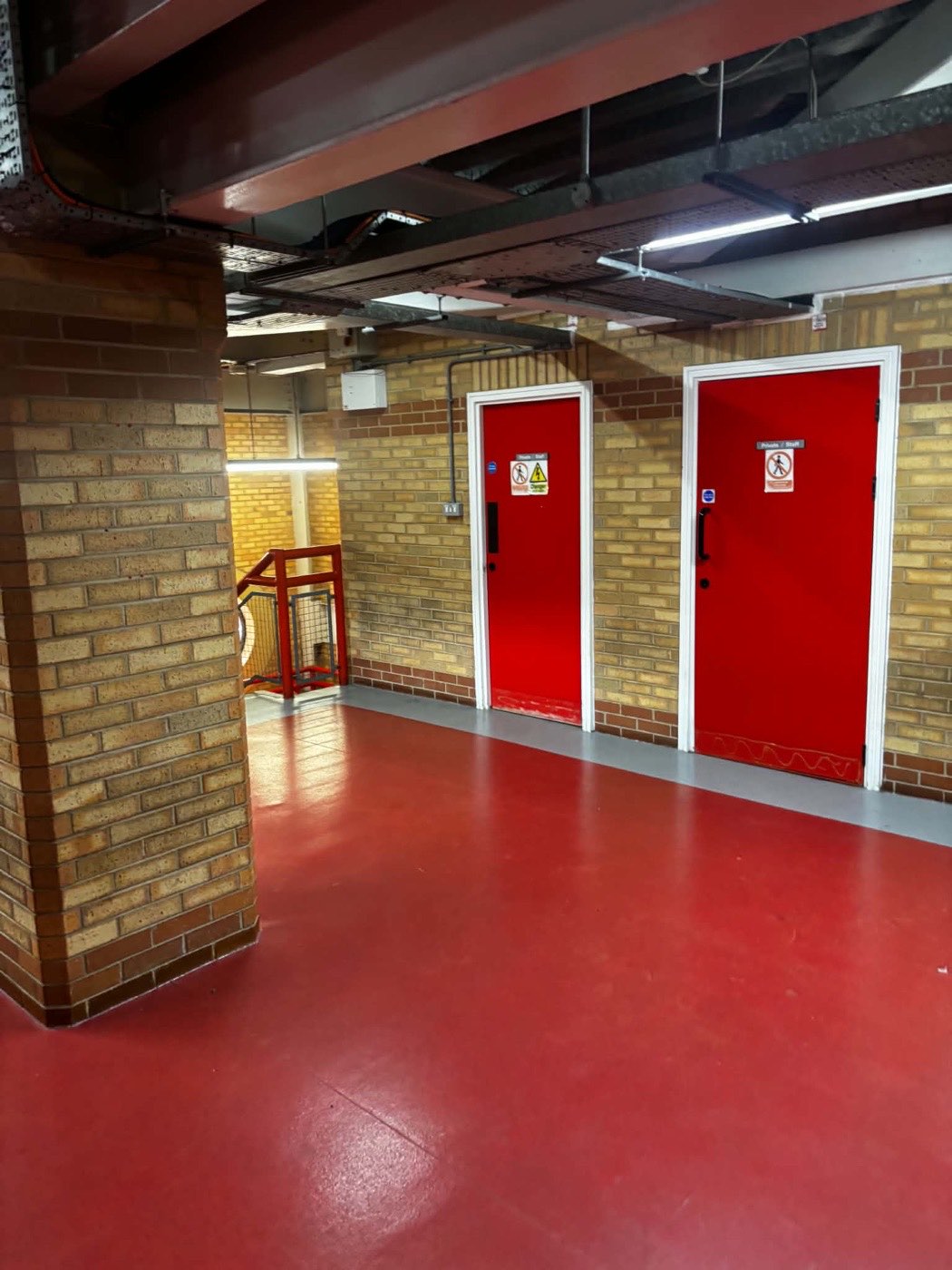 Freshly finished red fire doors and white frames on an Anfield concourse